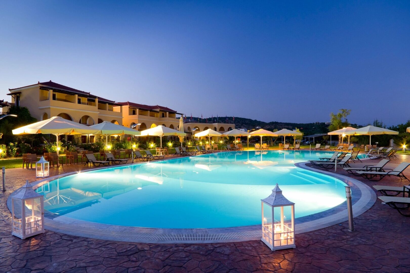 A pool with lights and umbrellas in the background.