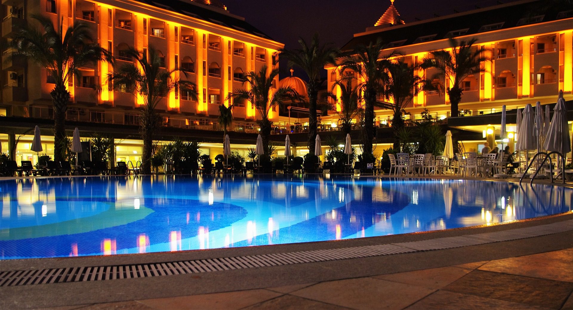 A pool with lights on in front of a building.