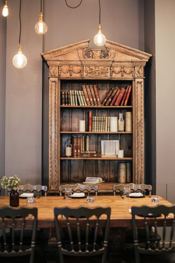 A wooden table with chairs and a book shelf.