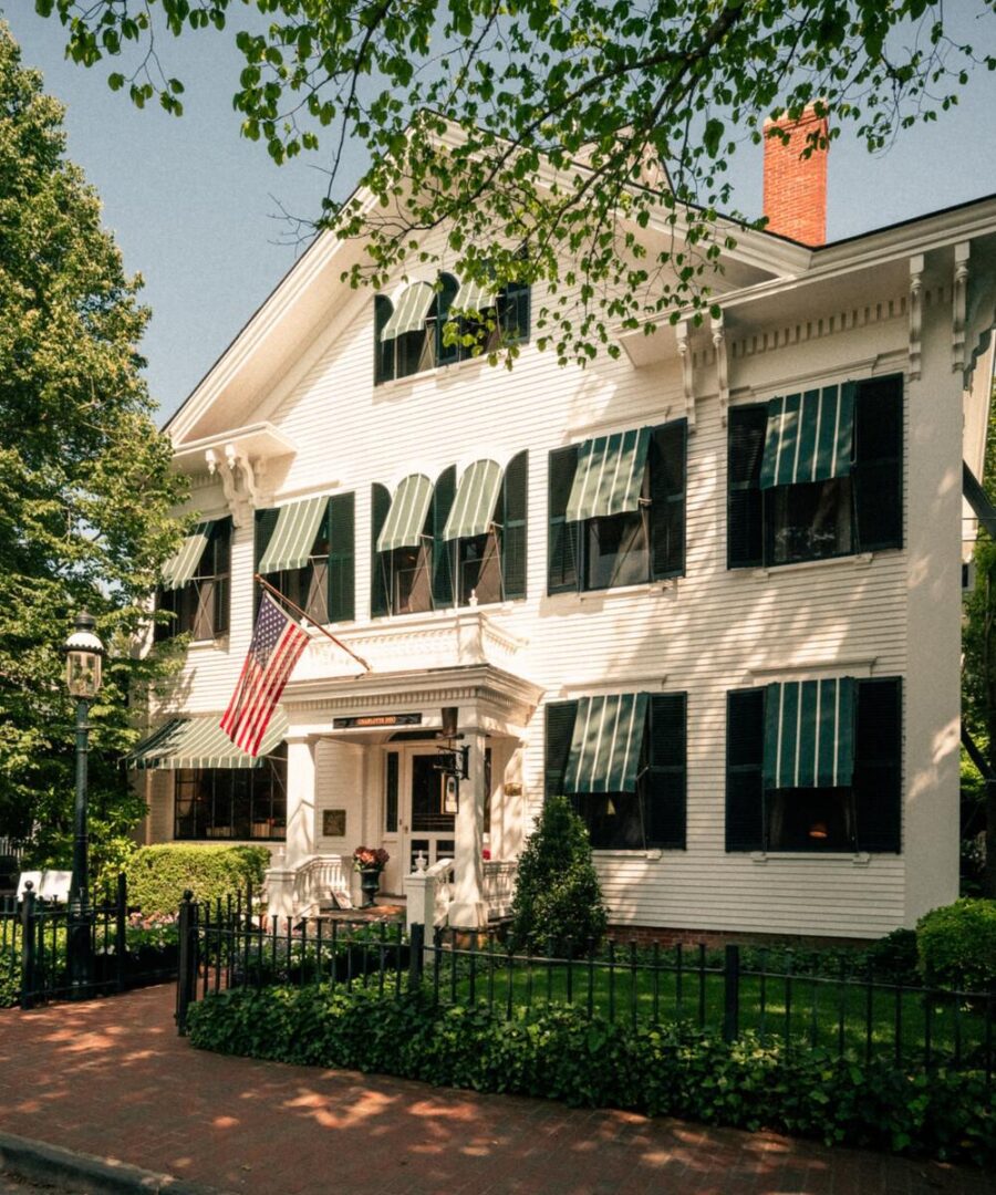 A white house with green shutters and american flag.